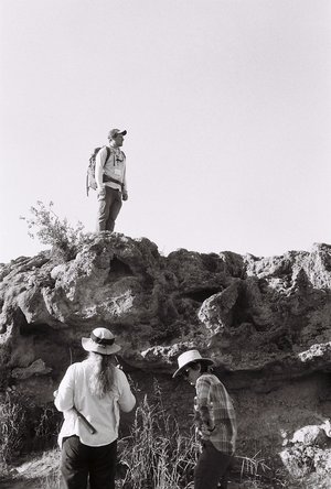 Photograph of a person standing atop a rock outcrop while two people stand below.
