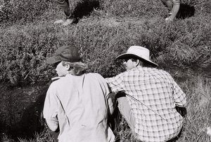 Photograph of two people crouched beside a small stream.