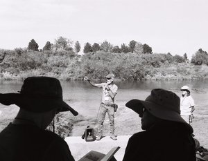 Photograph of a person holding a microphone and speaking to a small group of people.